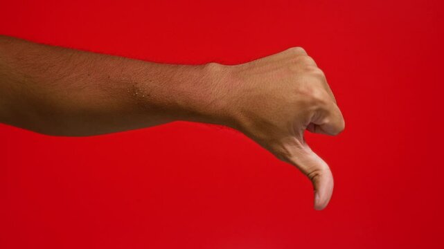 Man showing thumbs down hand gesture against a vibrant red background implying dislike and disapproval