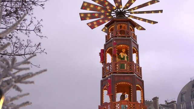A traditional German Christmas pyramid adorned with glowing lights, standing beautifully in a festive Paris market during the holiday season.