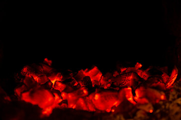 A close-up shot of glowing red hot coals in a fireplace. The fire has died down, leaving behind embers that still give off a warm glow.