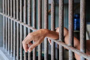 prisoner's hands behind bars with black background