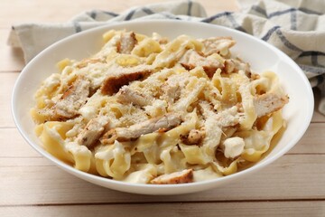 Tasty Alfredo pasta with chicken on light wooden table, closeup