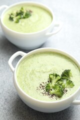 Delicious broccoli cream soup in bowls on light table, closeup