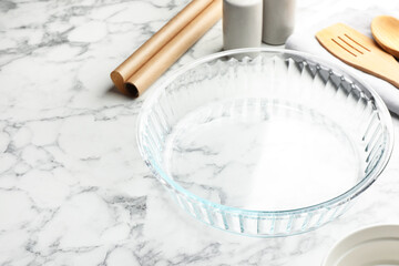 Glass casserole and other cooking utensils on white marble table, closeup