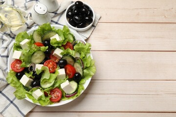 Delicious fresh Greek salad and ingredients on light wooden table, flat lay. Space for text
