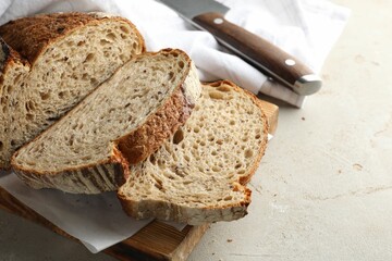 Cut loaf of fresh bread and knife on table, closeup