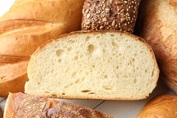 Whole and cut bread loafs on white table, closeup