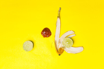 Ketchup, halved lime, and banana peel on a yellow backdrop