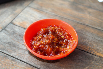 Portrait of sambal ulek or sambal terasi in small orange bowl on wooden table background.