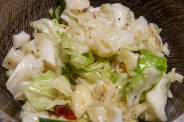 close-up of cooking or tempered cabbage dish, chopped cabbage mixed with mustard seeds, onions and red chili, preparing flavorful healthy food in soft focus