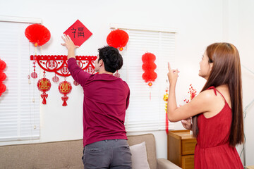 A couple decorates their living room for Chinese New Year, arranging red lanterns and festive...
