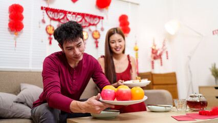 A Chinese couple prepares a festive table with traditional fruits and dishes, creating a warm and...