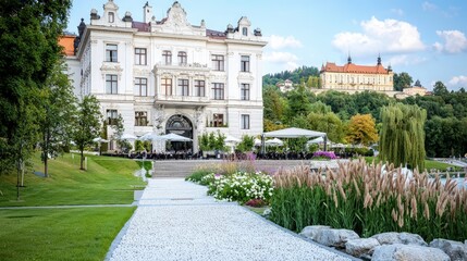 Elegant European building with outdoor cafe, garden, and hilltop castle in background.