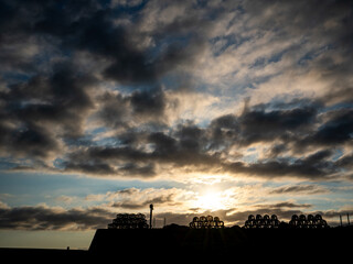 Lobster pots stacked on harbour wall at sunrise in silhouette