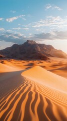Naklejka premium A breathtaking view of golden sand dunes under a clear blue sky, with rugged mountains in the background, capturing the serene beauty of a desert landscape.