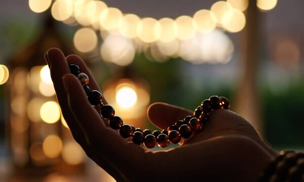 A hand holding a decorative bead bracelet against a sunset backdrop.