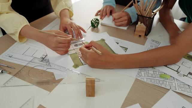Smart architect and safety engineer discussion about building blueprint on table with architectural document, measurement tools and wooden block scatter around at modern office. Closeup. Delineation.