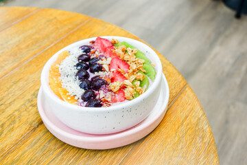Acai bowl with strawberries, blueberries,orange,kiwi fruit,granola ,chia seeds and coconut flakes on wooden background,close-up, top view, space for text.