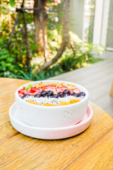 Acai bowl with strawberries, blueberries,orange,kiwi fruit,granola ,chia seeds and coconut flakes on wooden background,close-up, top view, space for text.