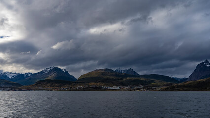 Beautiful mountain range. View from the ocean. Snow-capped peaks against a cloudy sky. The city of Ushuaia is located on the shore,at the foot of the hills.Ripples on the blue surface of the Channel  
