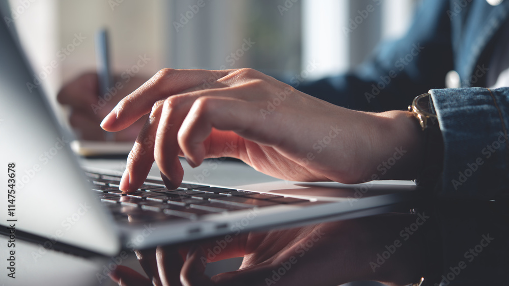 Poster close up, female student using laptop computer and writing notes in notebook while doing homework, e