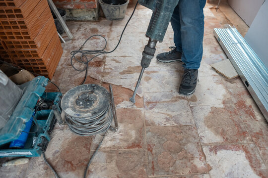 Trabajador demoliendo el suelo con un martillo electrico en reforma de casa interior.