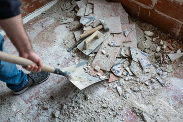 Worker picking up masonry debris with shovel after demolition.