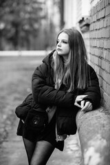 Portrait of a young beautiful long-haired girl in a dark dress in an urban environment. Black and...