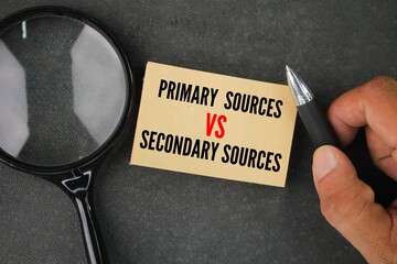 magnifying glass, pen and paper with the words Primary Sources vs Secondary Sources.