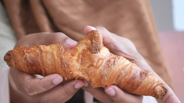 closeup of hand breaking a croissant bun 