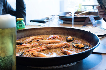 glass of blurred craft beer lager beer with Spanish Valencian paella of traditional rice with seafood with crayfish shrimps . seafood