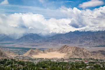 "Nestled Beauty: A Picturesque Town Cradled by Rugged Mountains and Snow-Capped Peaks Under a Dramatic Sky