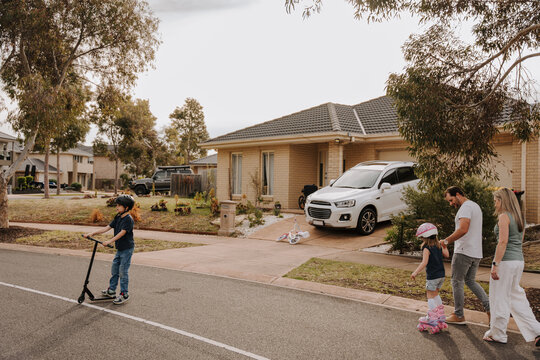 Two kids on the street with their parents one on scooter and the other on roller skates.