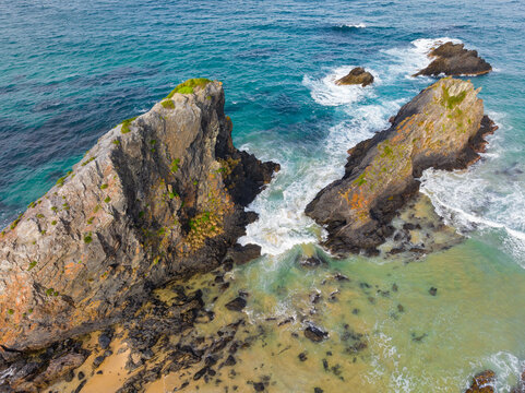 Aerial view of jagged rock formations off a sandy beach and rugged coastline