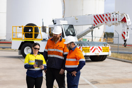 Workers working on digital tablet while standing in front of pick and carry crane machinery