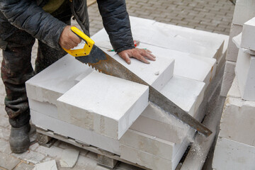 A man is cutting a block of white cement with a saw