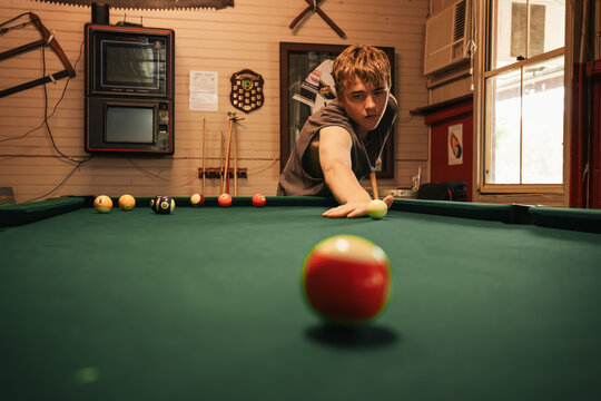 Teenage male playing 8 ball pool on billiard table in Australian pub