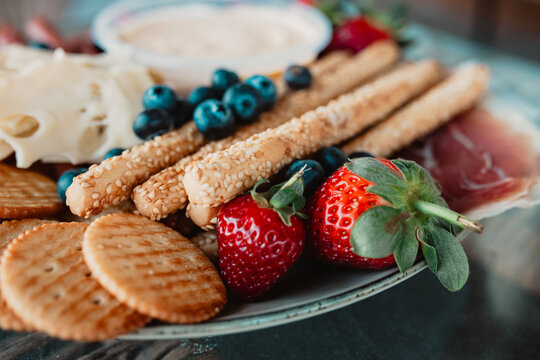 Vibrant appetiser platter with grissini, strawberries, blueberries, cheeses, and dips.