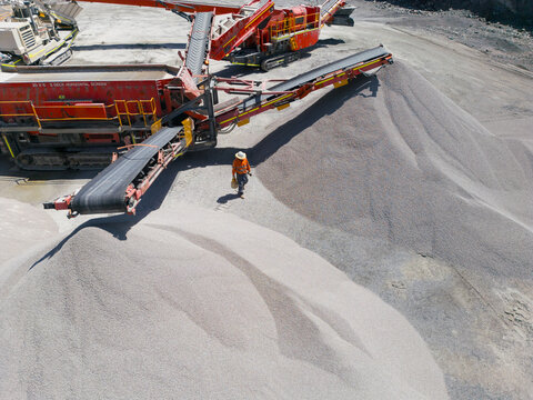 Man walking in between two piles of aggregates from the conveyor belt.