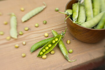 Still life with peas. Close-up. On an old wooden table is a saucer with unshelled pea pods, and next to them are open pea pods.