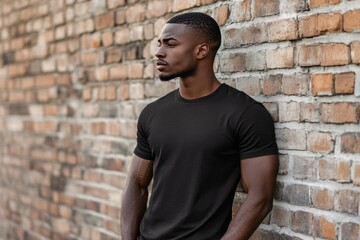 African American man in blank black t shirt against brick wall.