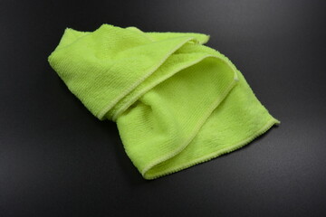 Bright lemon, yellow cloth, napkin, piece of synthetic microfiber fabric for wet cleaning in the house is located on a black plastic background.