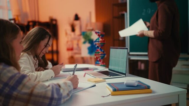 Two teen girls talk during a lesson, resulting in the teacher reprimanding them