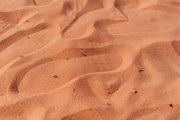 Wavy red desert sand surface featuring human footprints and natural textures under sunlight,...