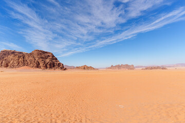 Wadi Rum Desert, Jordan. A stunning desert landscape featuring orange sand dunes, rugged rocky outcrops, and a vibrant blue sky..