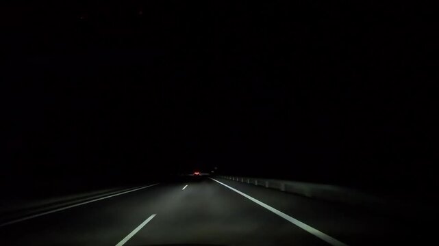 Driving on a two-lane road at night in darkness. View is from inside the car, with headlights illuminating the road ahead.