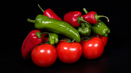Close-up image of tomatoes, red and green peppers on black background.
