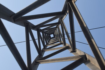 Steel structure of a high voltage pylon with wires, insulators blue sky and sun seen from...