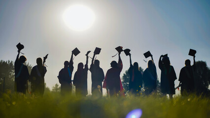 Silhouette of ten college graduates waving their caps at sunset.