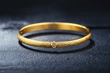 single golden bracelet displayed on smooth matte black surface under bright directional lighting