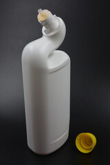 A white plastic bottle with a curved neck and a yellow cap is placed on a black plastic background. A plastic bottle is used for cleaning in the bathroom.